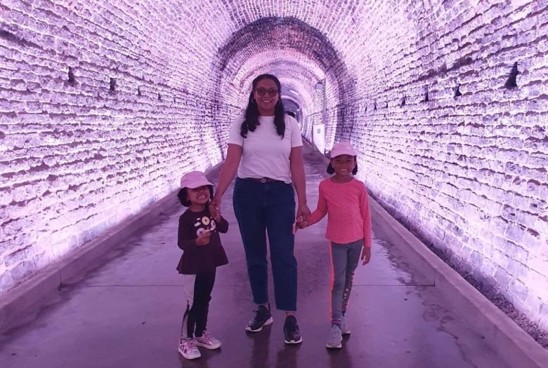 A woman holds the hands of two young girls in a lit train tunnel