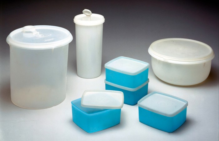 A variety of Tupperware containers from the 1980s, including a large cylindrical container with a lid, a tall cylindrical container with a flip-top lid, a round container with a lid, and four rectangular containers, three of which are stacked. The containers are primarily translucent white and blue.