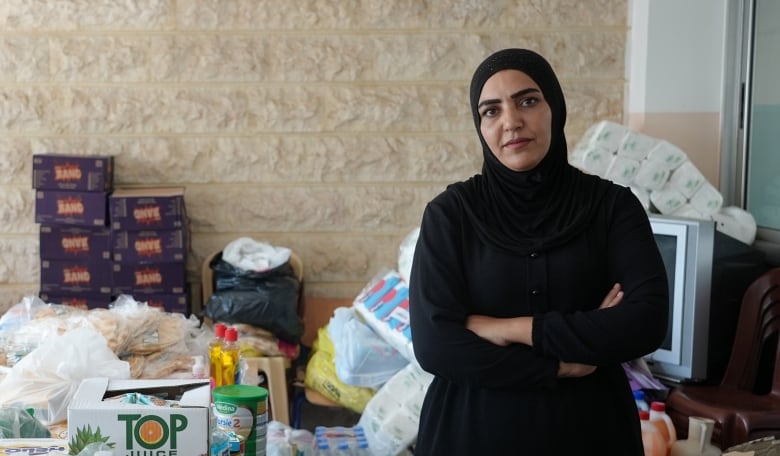 A woman wearing black sits with her arms crossed near food and water supplies.