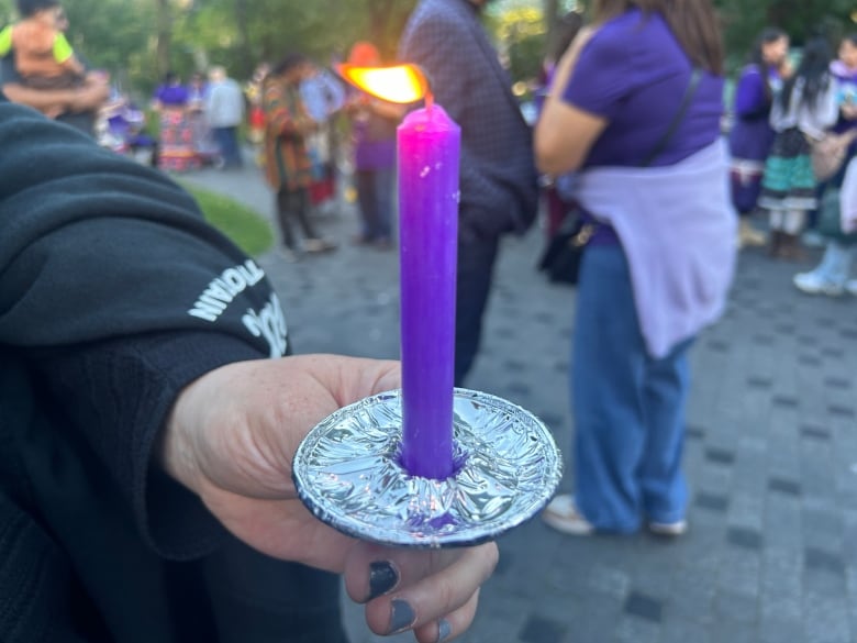 A close up of a woman holding a lit purple candle.