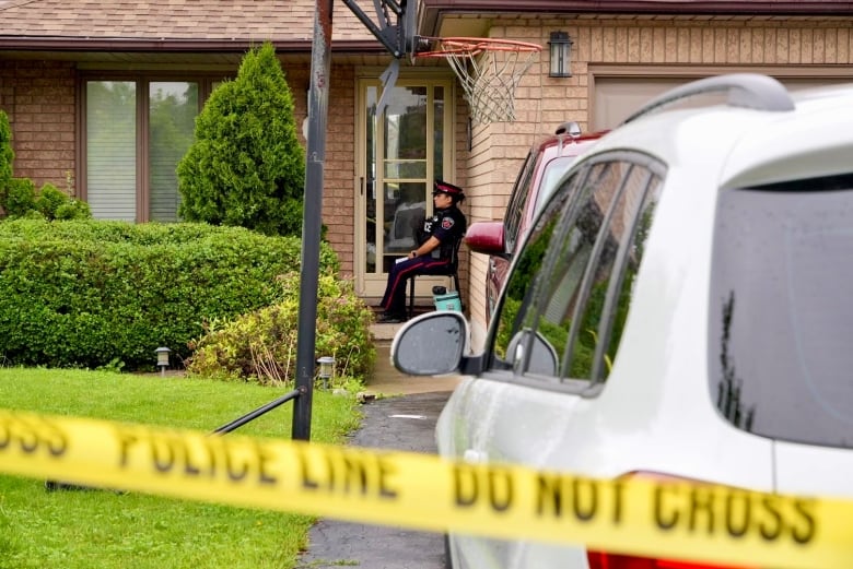 A Hamilton police officer sits outside the door to a home where, police say, a 16-year-old was stabbed during a family gathering.