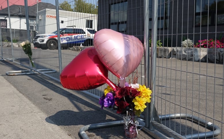 Two heart-shaped balloons and a bouquet of flowers on a fence around a closed building in summer.