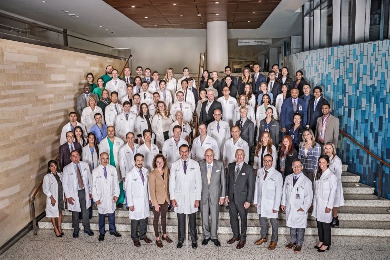 More than 100 people, most wearing lab coats and some wearing suits, stand on a staircase.