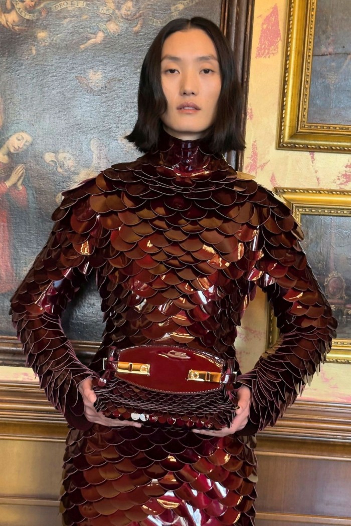 A dark haired woman models a red-brown dress with scale-like texture