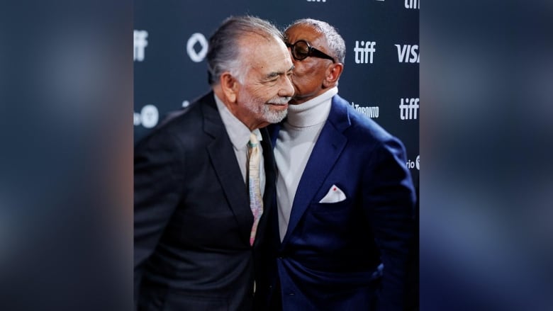 An actor kissing a director on the cheek during a TIFF red carpet.