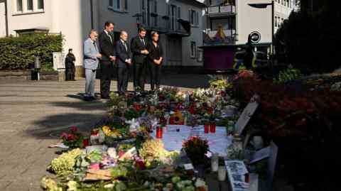 Herbert Reul, Hendrik Wuest, Olaf Scholz, Tim Kurzbach, and Mona Neubaur stand at a makeshift memorial for the victims at the site of a knife attack in Solingen, western Germany, on August 26, 2024. The memorial is adorned with flowers, candles, and messages.