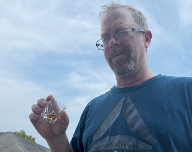 A man holding a shot glass winces.