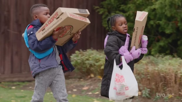 Two children have their hands full walking as their arms are laden with pizza boxes and plastic bags.