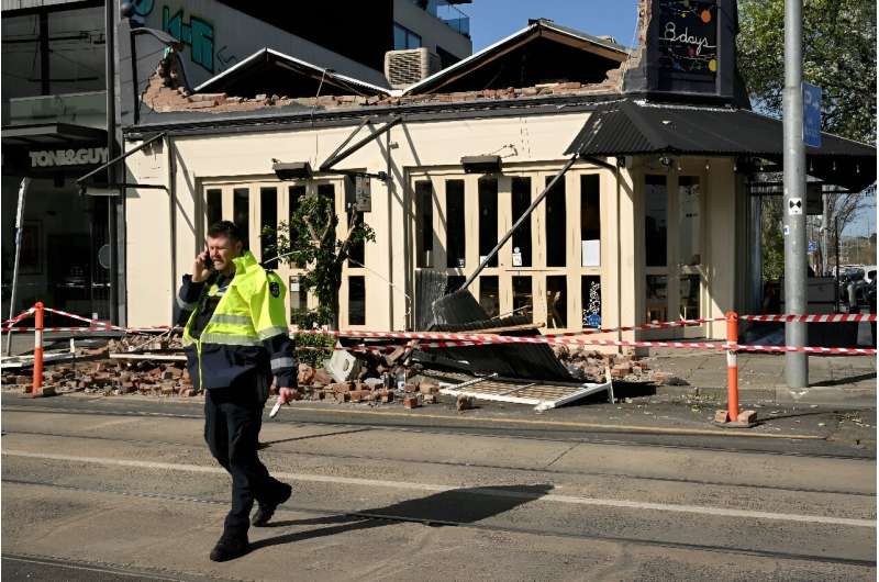 A policeman walks past the collapsed facade of a building in Melbourne as wild storms batter Australia