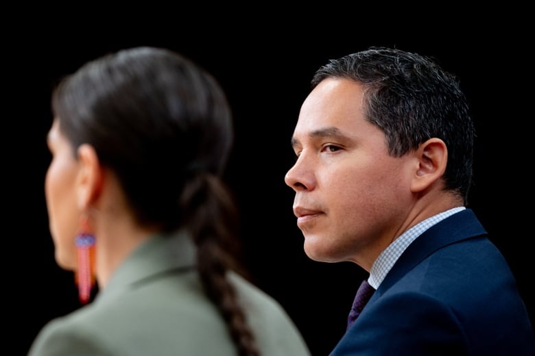 One political leaders looks left at another leader speaking at a news conference.