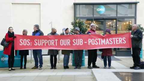 A line of protesters hold a long red banner reading “SOS - Support our sub-postmasters”