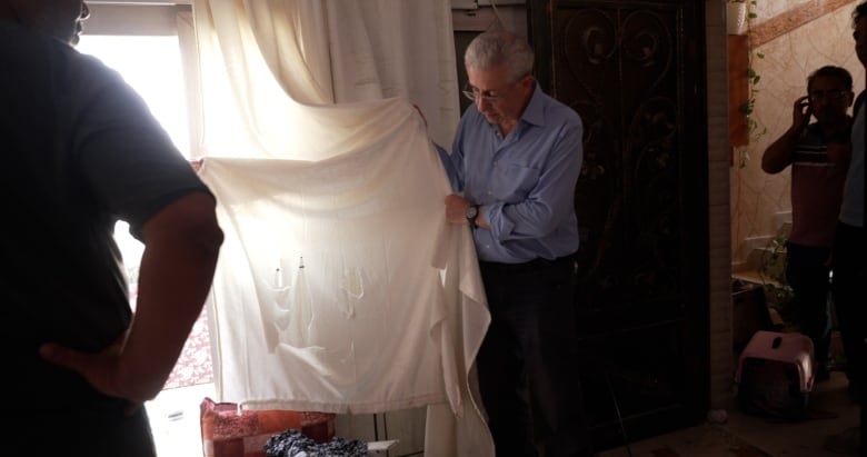 A person in a home holds up a curtain that is damaged with rips.