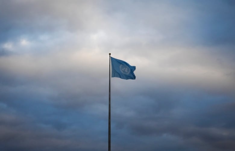 A United Nations flag flies at UN headquarter against an overcast sky. 