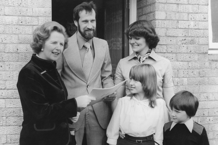 The family of four stand next to Mrs Thatcher in the doorway of the house as she passes the documents over. The image is black and white