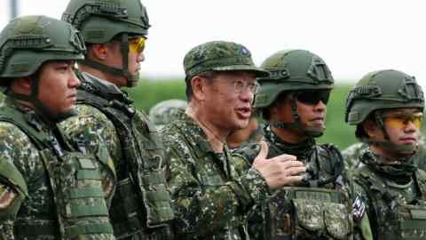 Wellington Koo speaks while standing among several soldiers during missile shooting exercises in Fangshan, Pingtung County, Taiwan. The soldiers are dressed in camouflage uniforms and helmets, and some are wearing protective goggles.