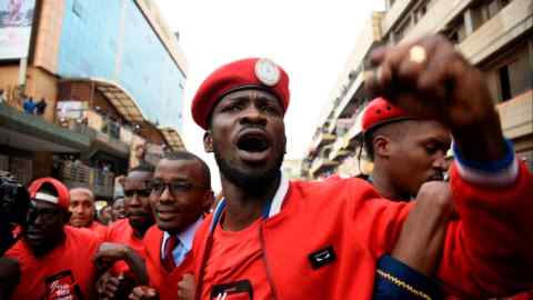 A man wearing a red uniform with beret stands amid demonstrators in a street, shaking his fist