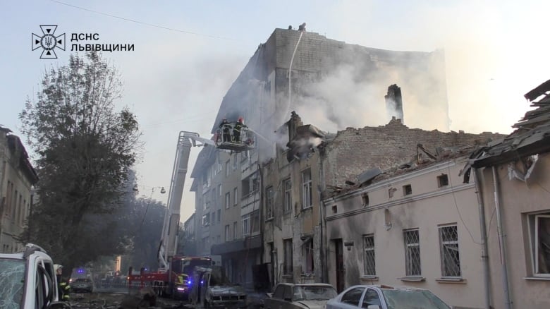 Smoke rises from a damaged low-rise building as a ladder is shown extending from a fire truck, with at least two firefighters utilizing a hose against the building.