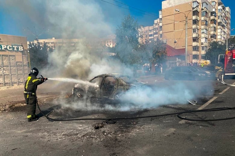 A firefighter sprays water on a destroyed car.