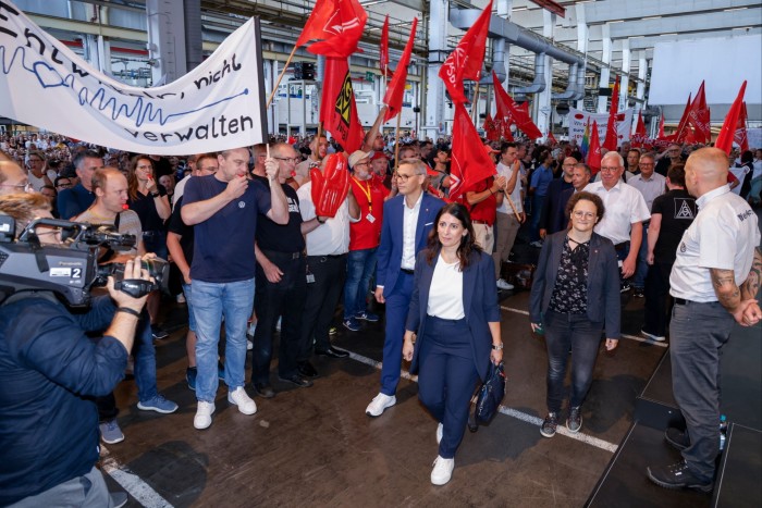 Daniela Cavallo walks through a crowd of people holding red flags and banners at Volkswagen’s Wolfsburg headquarters.