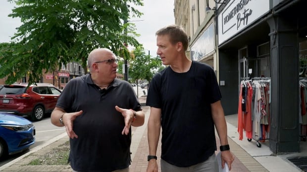 Two men, dressed in black shirts, walk side-by-side down a downtown street.