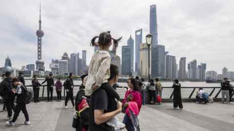 People are seen walking and standing along the Bund in Shanghai, with the iconic buildings of Pudong's Lujiazui Financial District visible in the background on May 1 2024