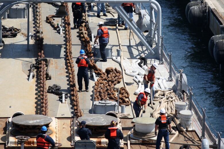 Port workers pull large chains at a dock.