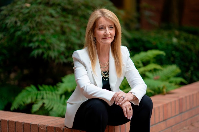 A middle-aged woman in a suit sits on a wall