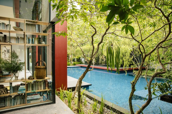 A blue pool lies to the right of a modern house, and is surrounded by trees