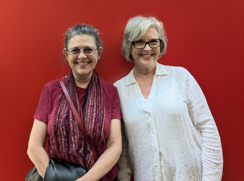 Two women stand against a red background