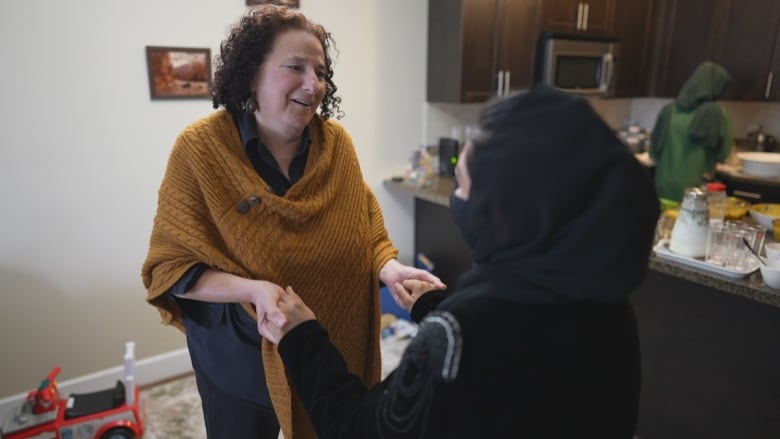 Two women are holding hands. Only one woman's face is visible and she is smiling.