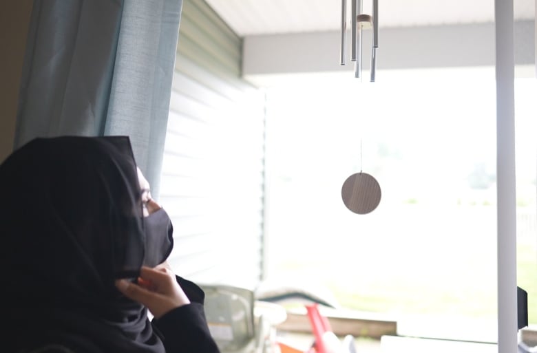 A woman wearing a headscarf looks out a window.