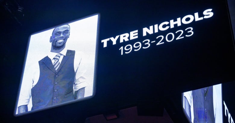 A picture of a smiling man is lit up next to the words "Tyre Nichols 1993-2023" on a black backdrop. 