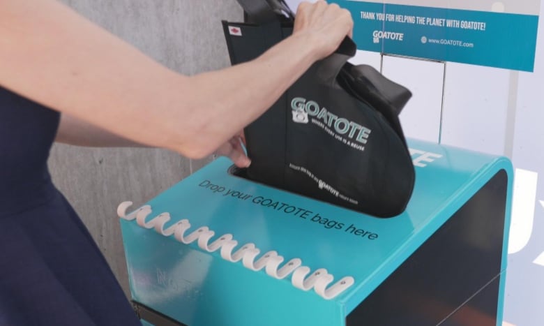 A woman putting a reusable bag in to a return bin. 