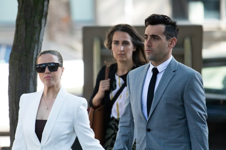 A man wearing a light suit and black tie walks near to two women