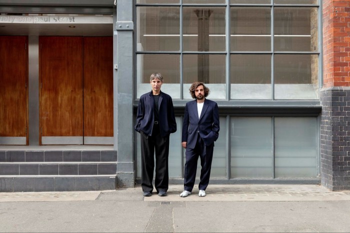 Two men stand outside a London building, which looks like a repurposed factory from the early 20th century 