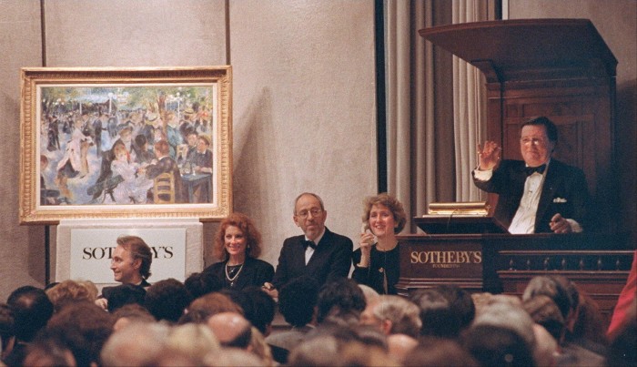 A male auctioneer in black tie presides over a Sotheby’s auction room with Renoir’s painting on display