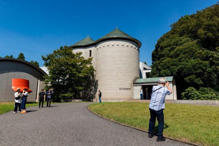 A man takes a photo of a building that resembles a round castle tower set amid lawns