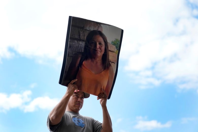 A man holds up a large photo of a woman.