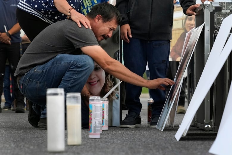 A man reaches to touch a large photo with candles in the foreground.