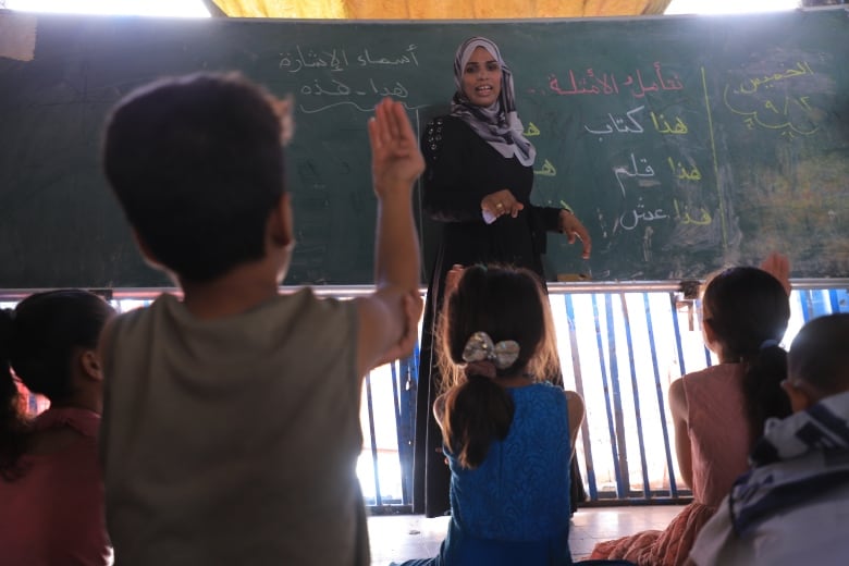 A woman stands at a chalkboard in front of students