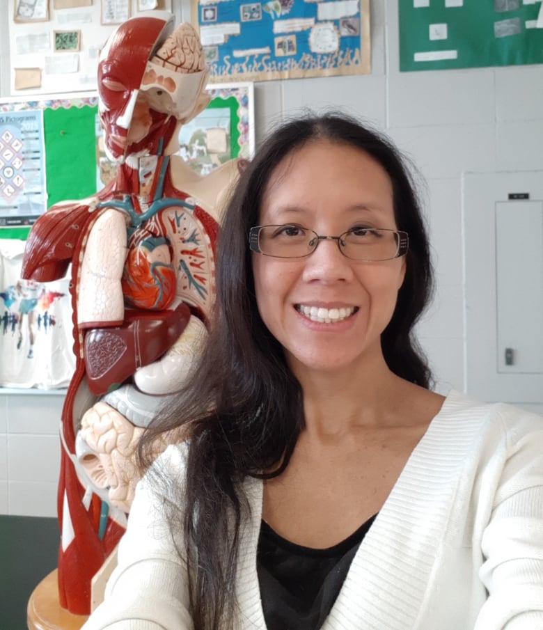 A smiling woman poses for a selfie next to a life-sized teaching model of the human body that shows all the major organs. 