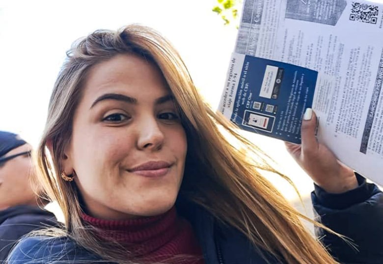 A smiling woman with long hair holds up a document for a selfie. 