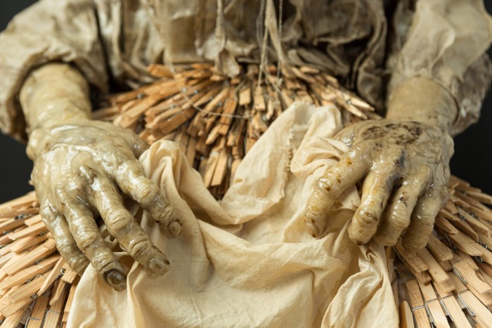 Three-dimensional multi-media artwork , made from cotton, wax, resin, wire and found objects. A woman is slumped, headless, over a tin bath of washing. Her dress is made from clothes pegs and her hands and feet are gnarled and calloused