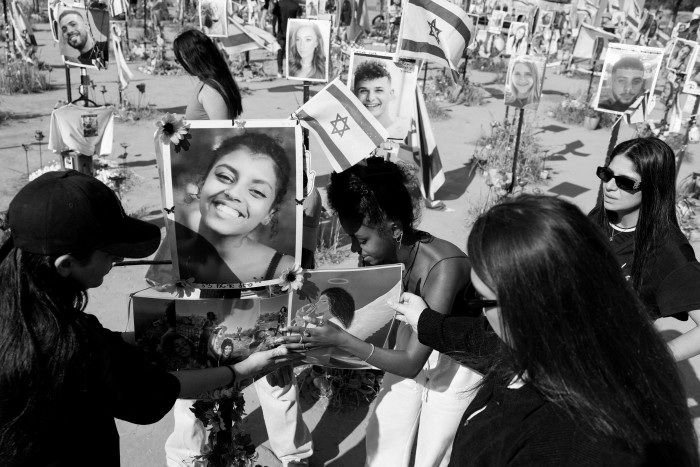 Young people push a post into the ground with a photo of a smiling person on it. Behind them is a whole field of similar posts with pictures of other victims