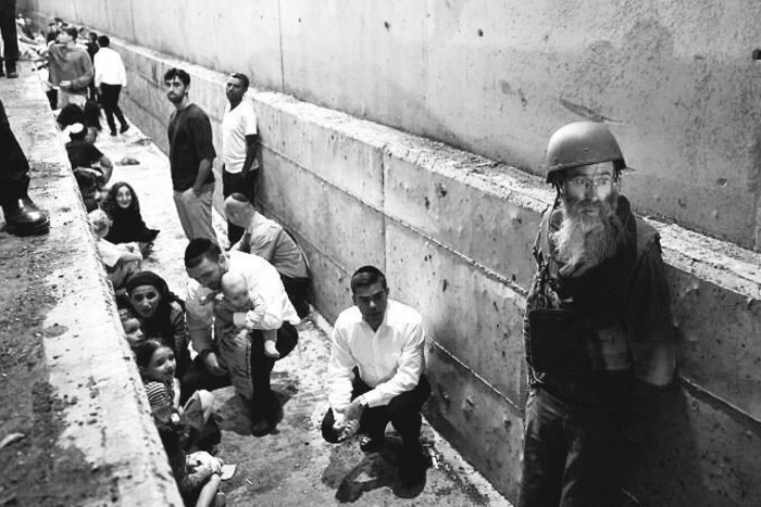 Anxious looking people shelter against a wall 