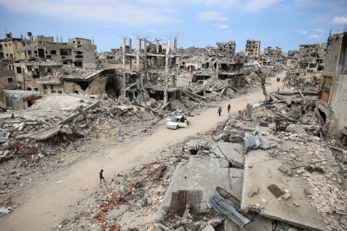 Displaced Palestinians walk past ruined buildings in Gaza City