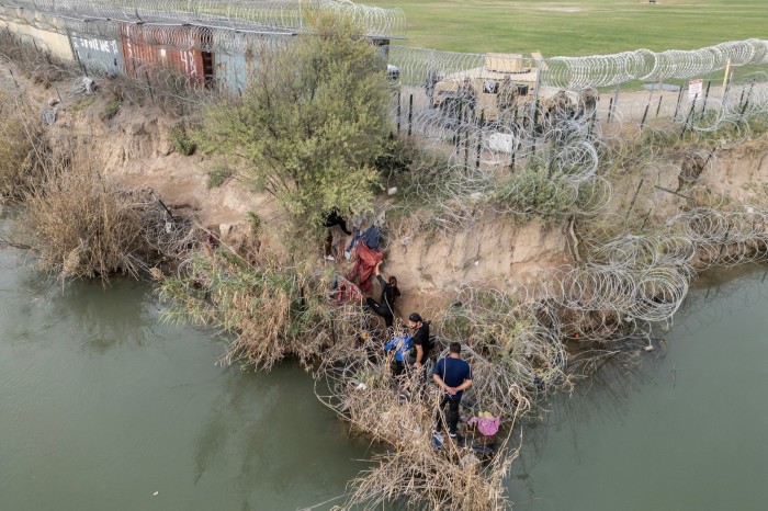 A group of migrants try to go through a wire fence on the banks of the Rio Grande river near US National Guard member