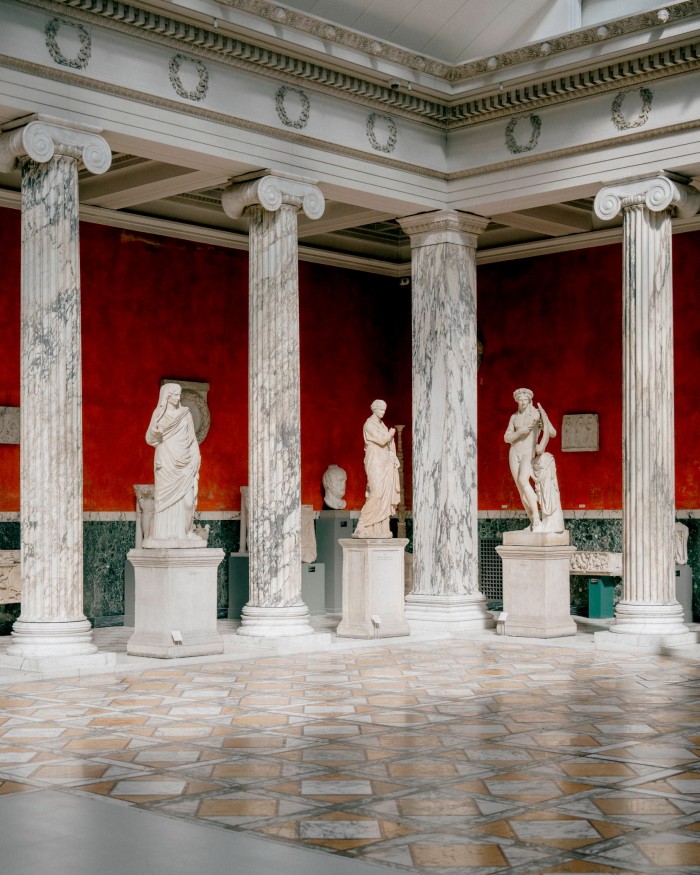 Classical sculptures in between marble columns in a red-walled room in Copenhagen’s Ny Carlsberg Glyptoket 