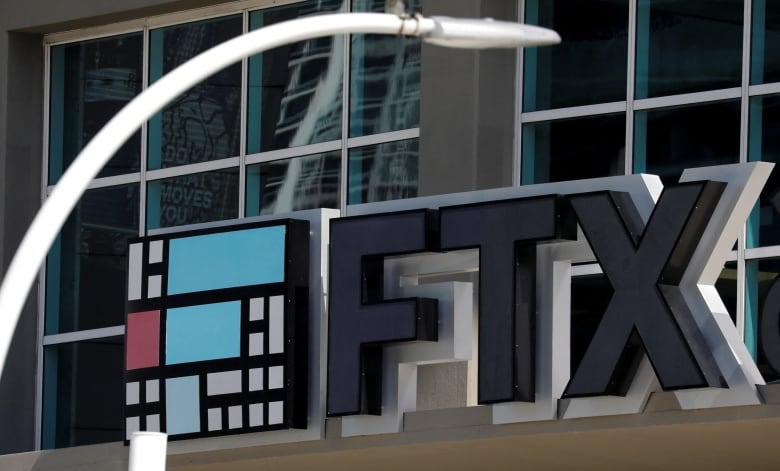 Big 3D black letters spell out FTX on the side of a building. A blurry white lamppost is visible in the image in front of the building facade. 