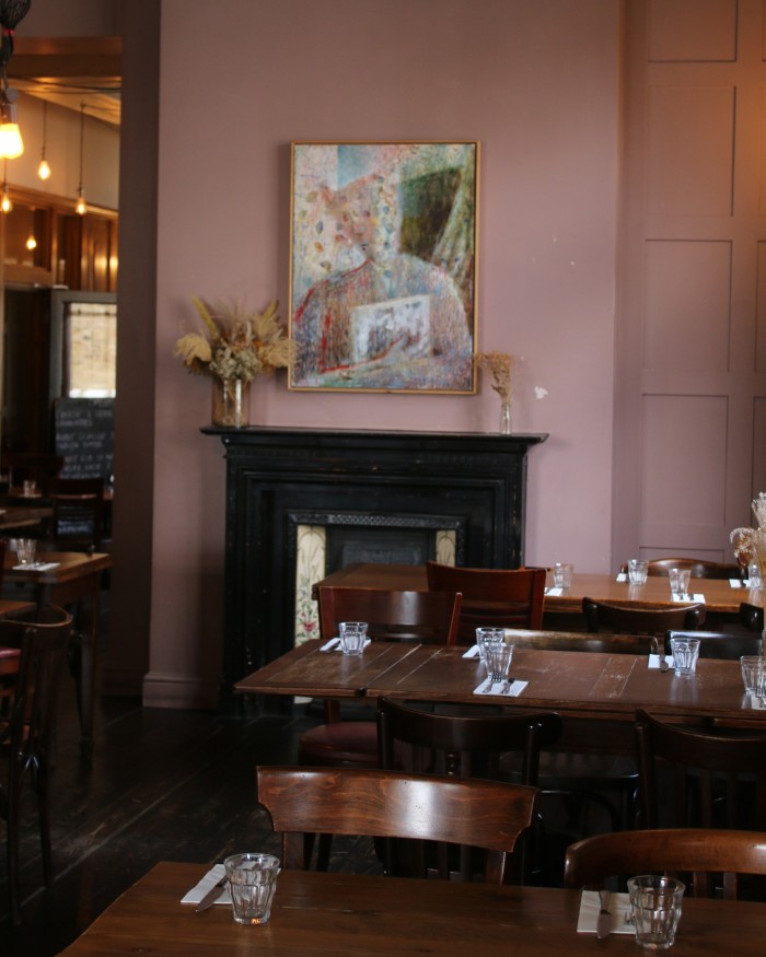 Dark-wood tables and chairs in front of a fireplace above which hangs an abstract artwork of a female figure at the Canton Arms